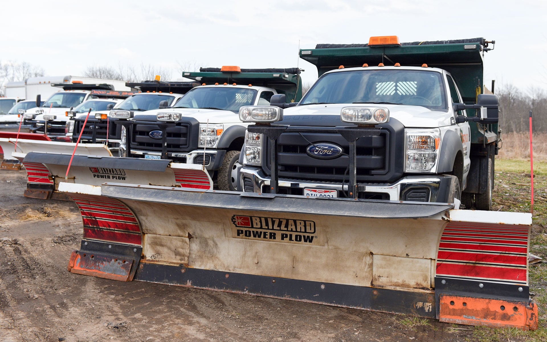 A row of plow trucks with blades staged in the O'Bryan Grounds Maintenance yard