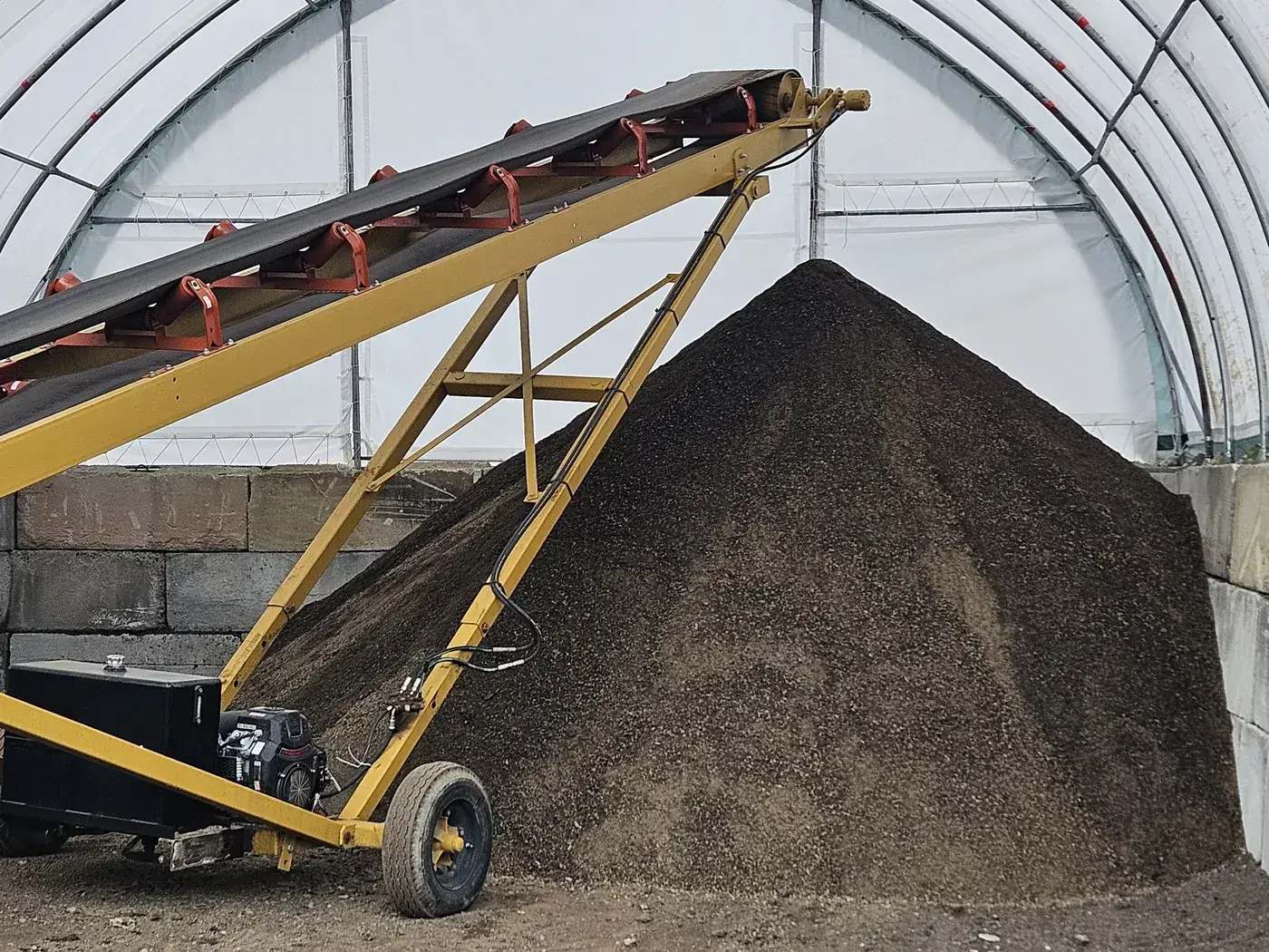 A conveyor stacking a cone of dark screened material inside a covered storage building