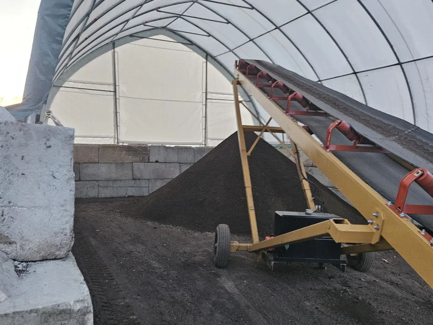 A stockpile of dark screened material held under a covered hoop building at the yard
